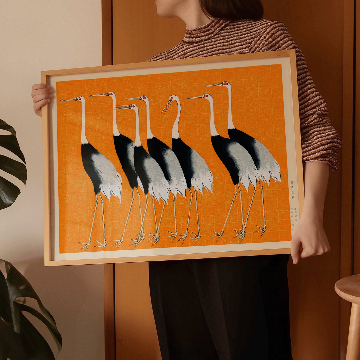 Vintage Japanese art print of cranes on orange background, framed in nude oak, held by person; museum-quality fine art piece.