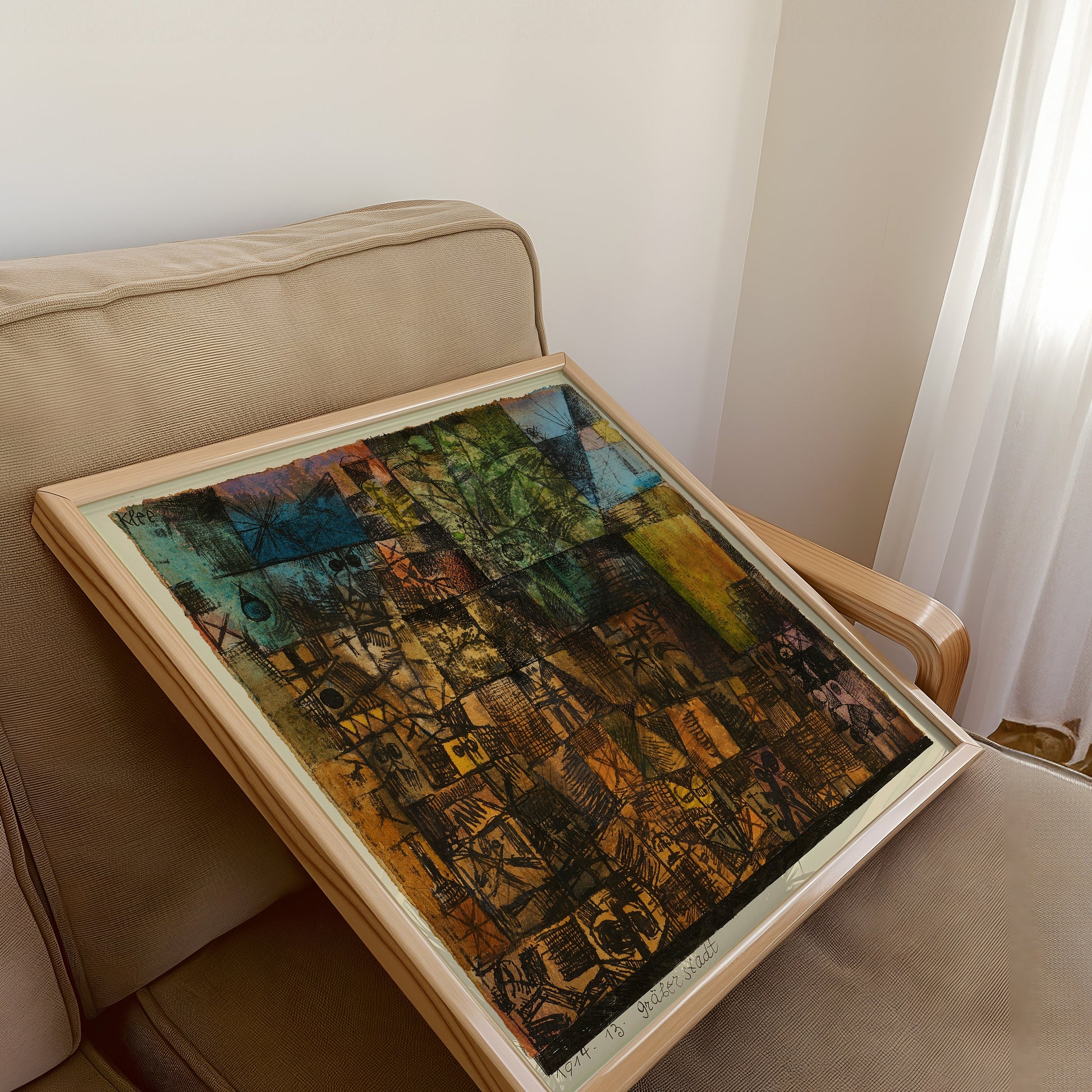 Vintage mid-century modern abstract art print by Paul Klee, City of Graves, framed and resting on a beige armchair.