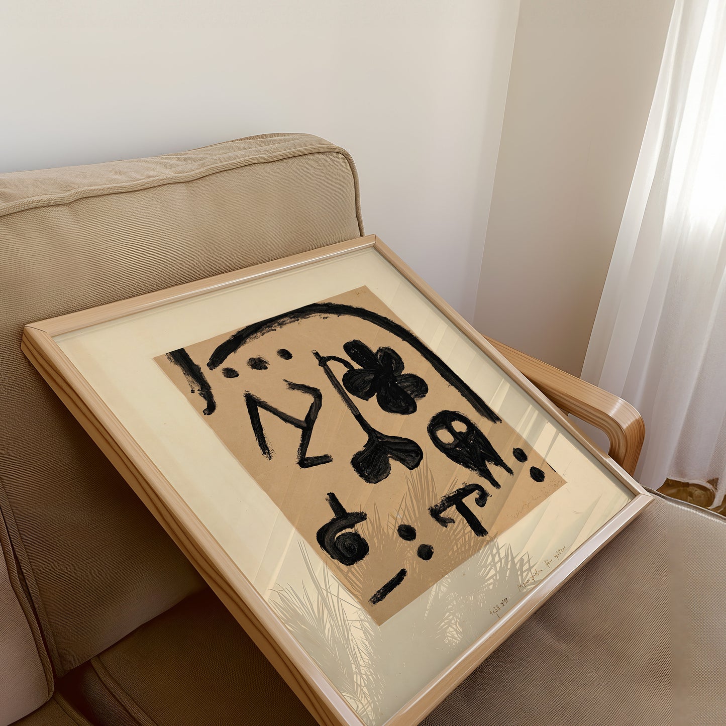 Vintage mid-century modern abstract art print in beige by Paul Klee, featuring bold black symbols, displayed in a wooden frame on a beige sofa.