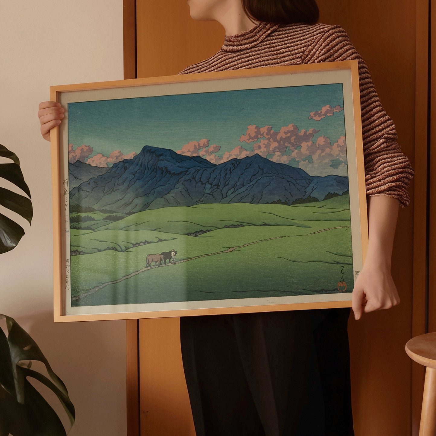 Person holding Kawase Hasui's "Dusk at Aso" framed Japanese woodblock print, featuring serene landscape scenery.