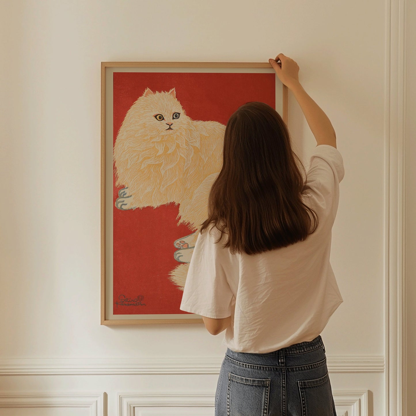 Woman hanging vintage Japanese woodblock print of a white cat in red frame on a wall.