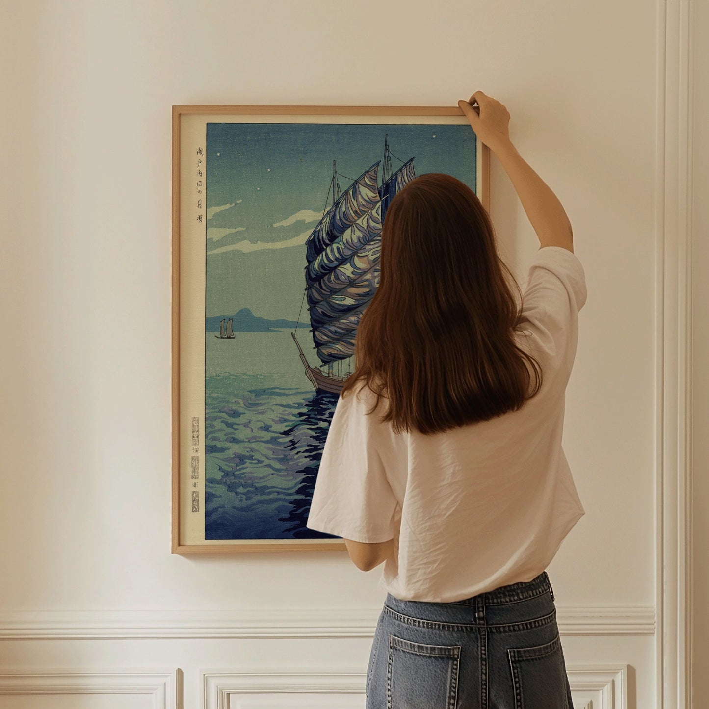 Woman hanging "Moonlight Over the Inland Sea, Seto" vintage Japanese woodblock print on wall.