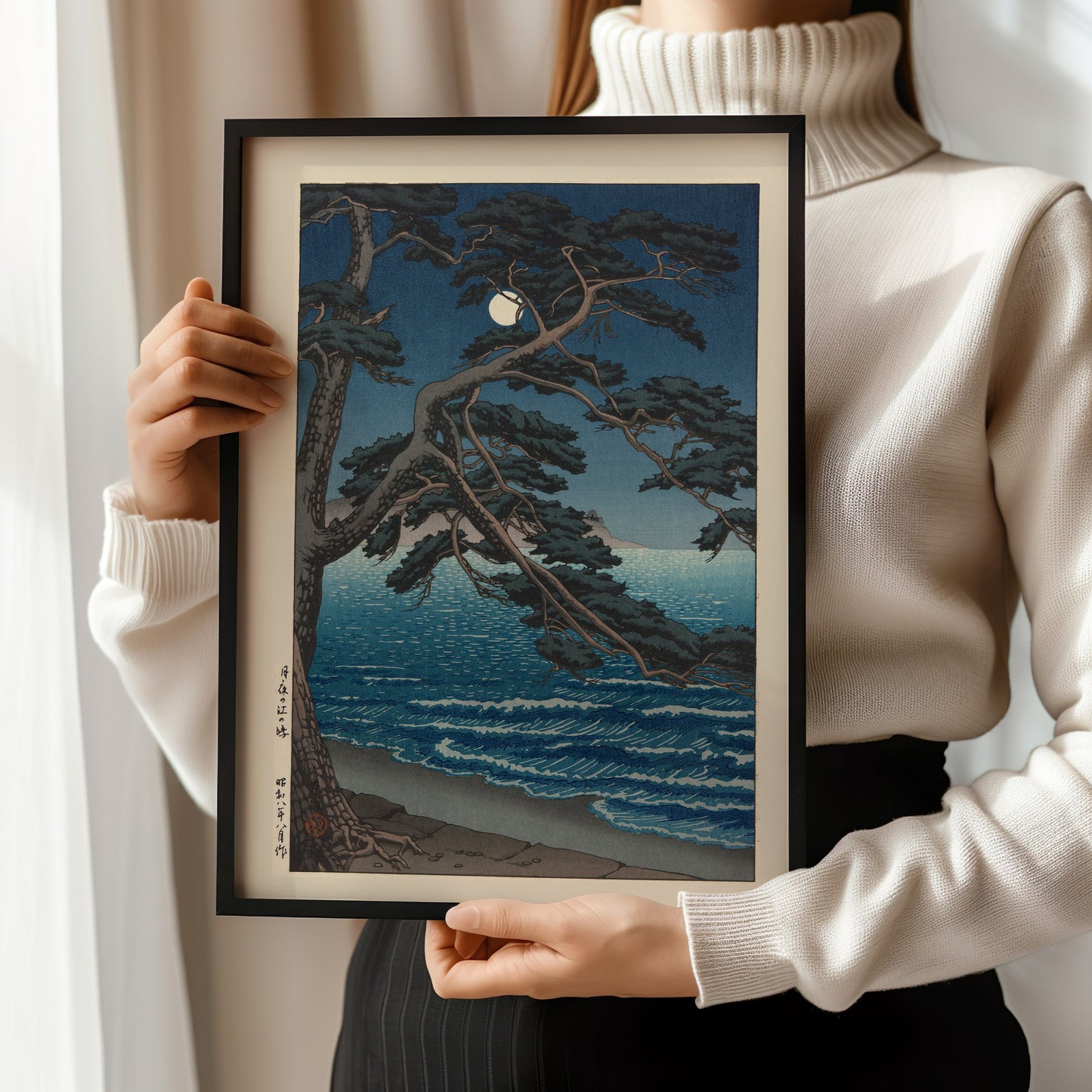 Kawase Hasui framed woodblock art print, Moon at Enoshima Beach, held by woman in white turtleneck sweater.