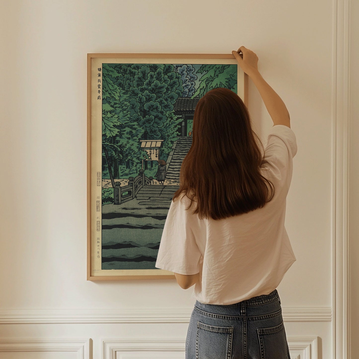 Woman hanging Shiro Kasamatsu In Front of Engakuji Temple print on wall, vintage Japanese woodblock art, framed in light wood.