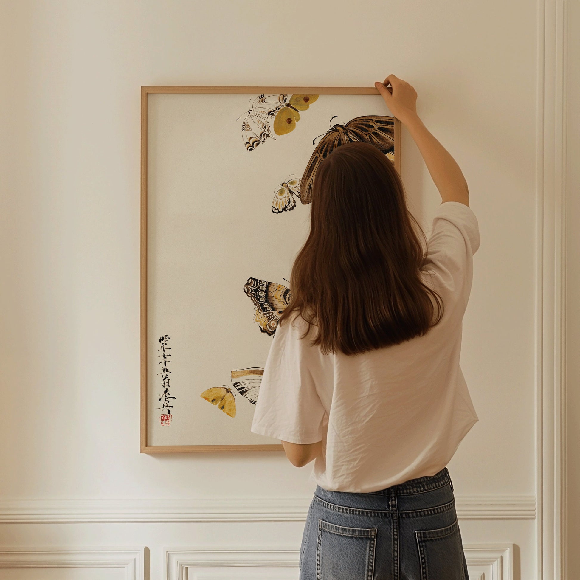 Woman hanging Shibata Zeshin vintage Japanese woodblock art print with butterflies in a handcrafted frame.