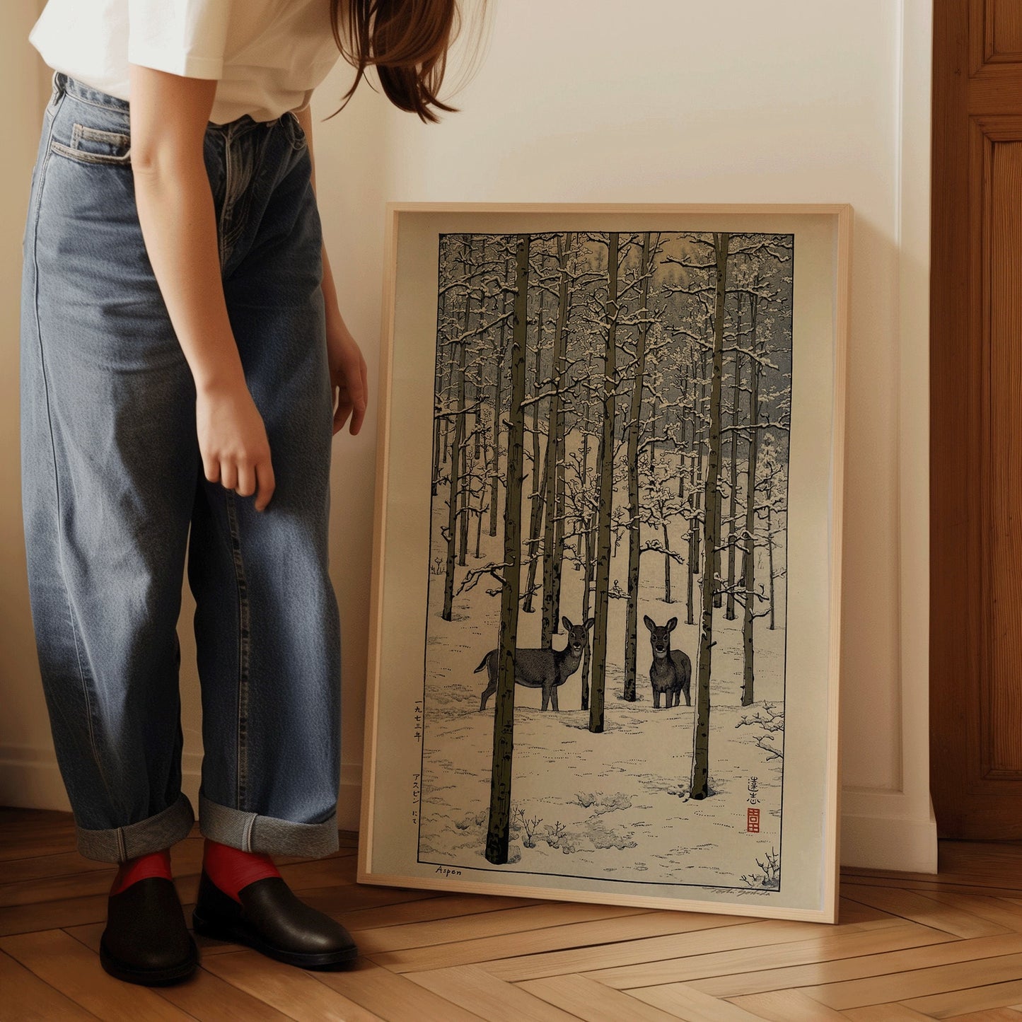 Woman admiring a framed vintage Japanese woodblock print of deer in a snowy forest.