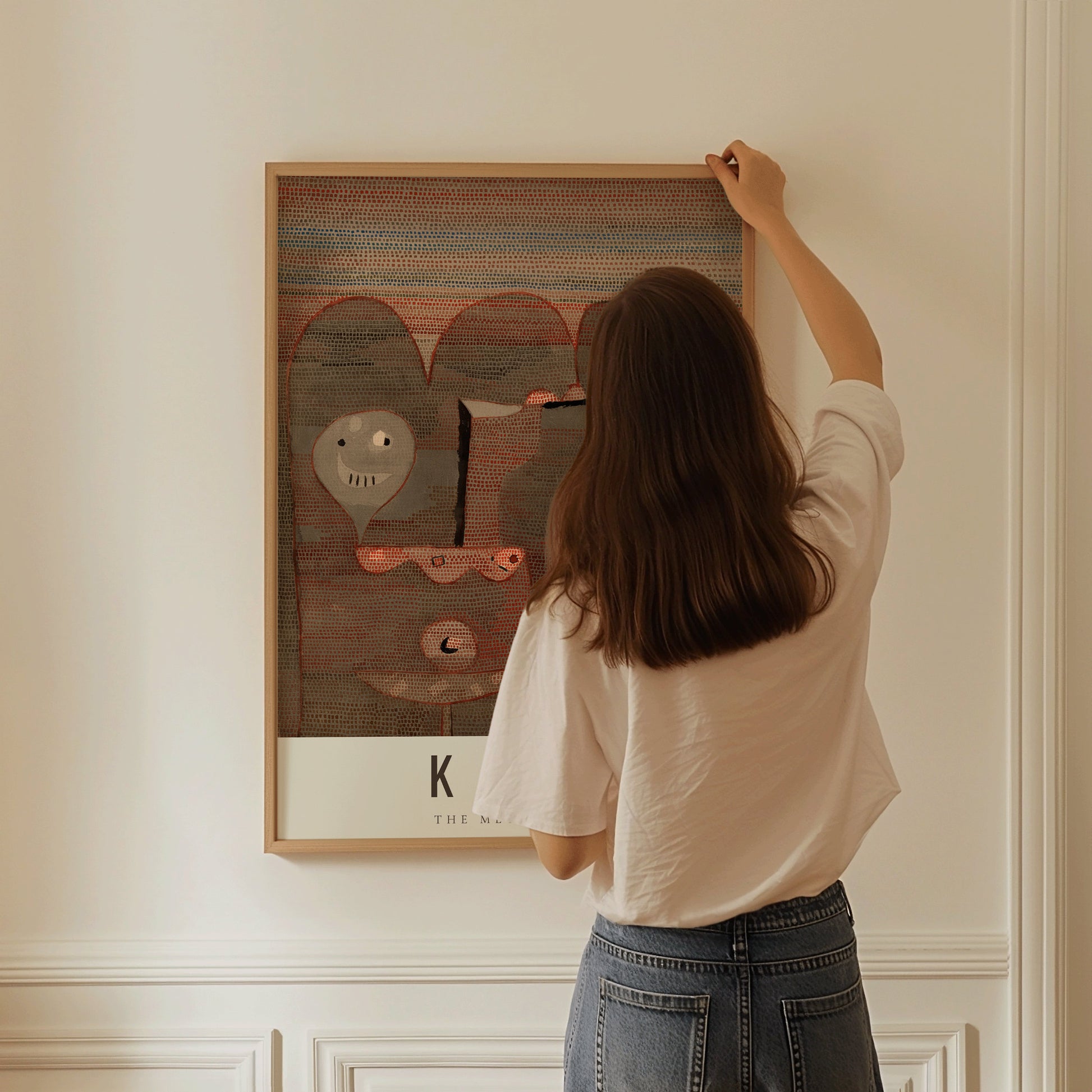 Woman hanging framed Paul Klee Barbarian Sacrifice modern abstract art print on a wall.