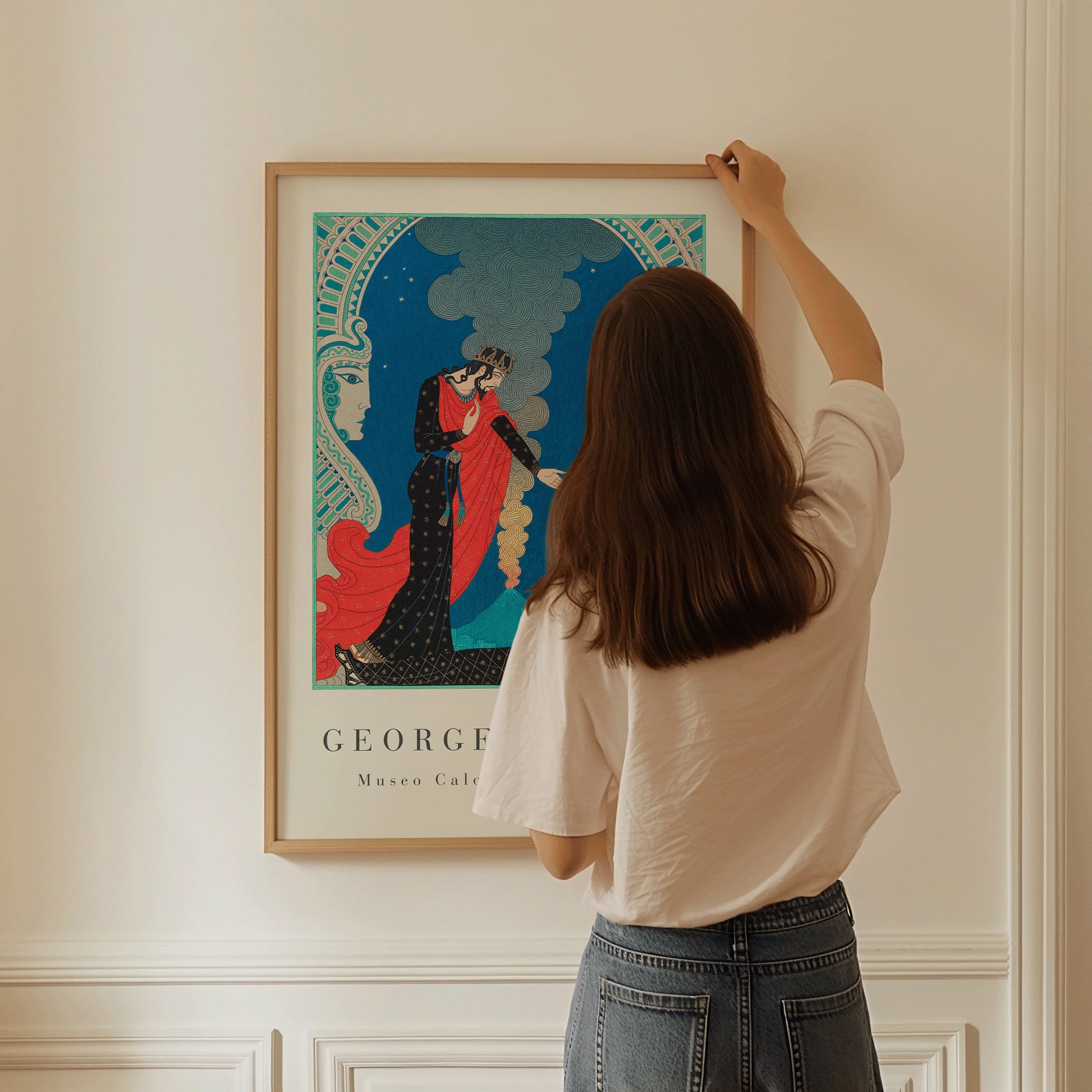 Woman hanging George Barbier's Emodecles and Pantea Art Deco print on beige wall, framed and ready to enhance home decor.