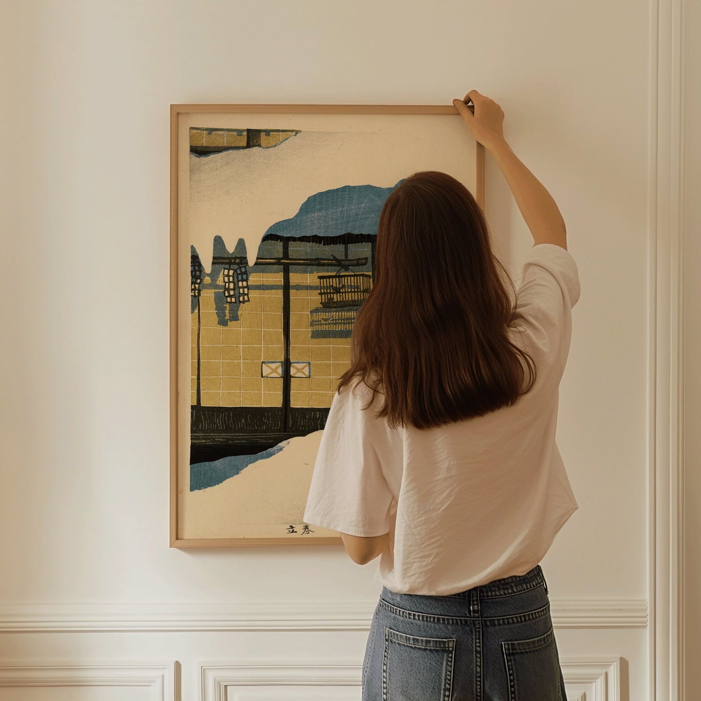 Person hanging vintage Japanese woodblock art framed in oak on wall.