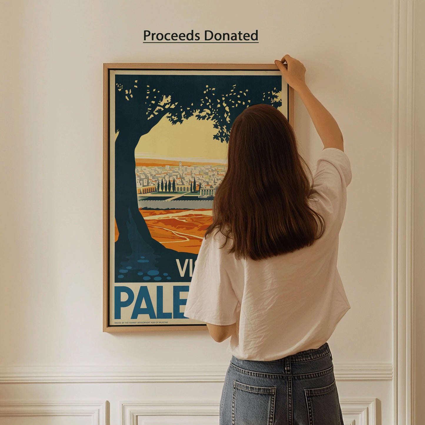 Woman hanging framed Visit Palestine poster, proceeds donated to Palestine Children's Relief Fund. Vintage art print for sale.