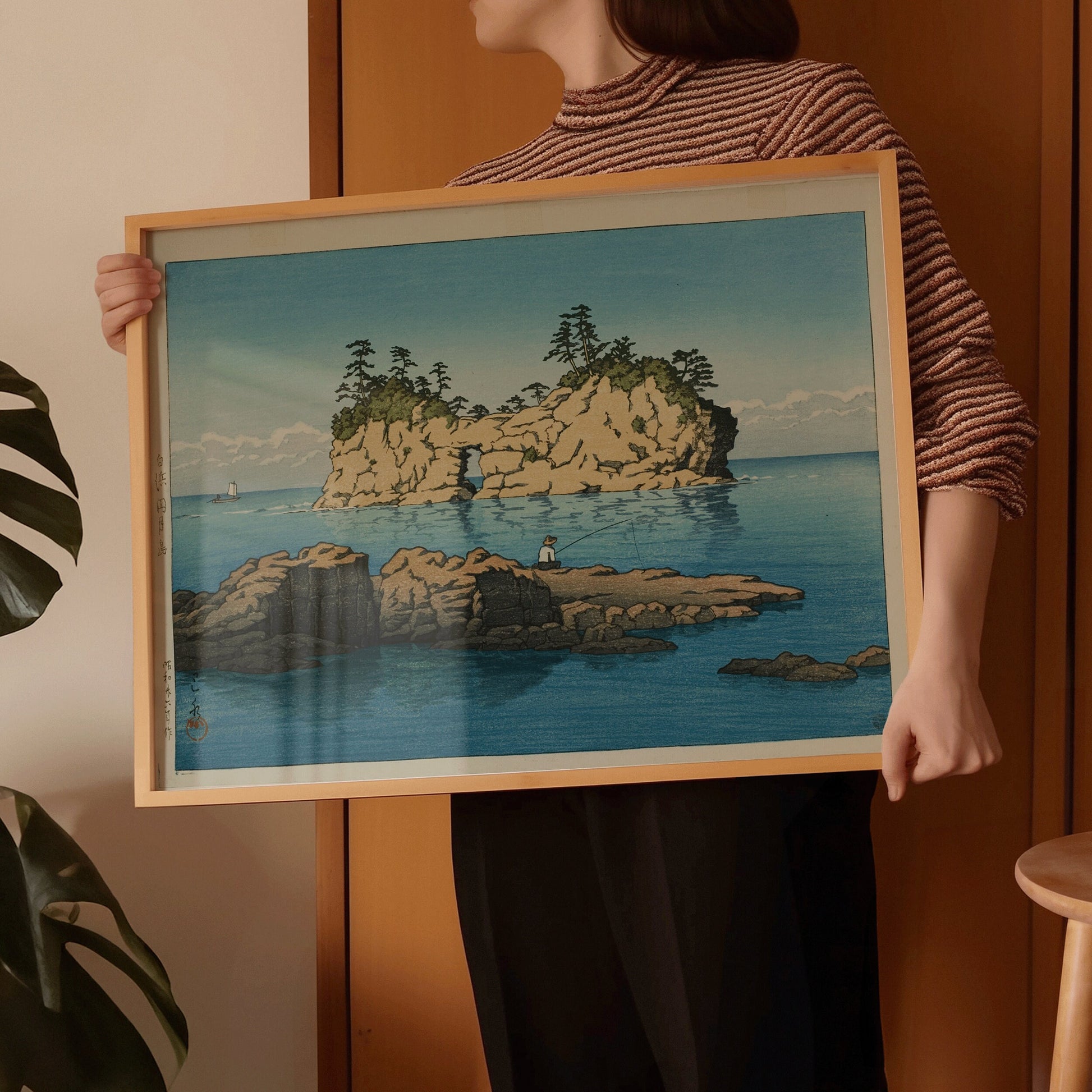 Person holding framed Kawase Hasui Engetsu Island Japanese vintage art print, showcasing elegant blue seascape with rocky outcrop.