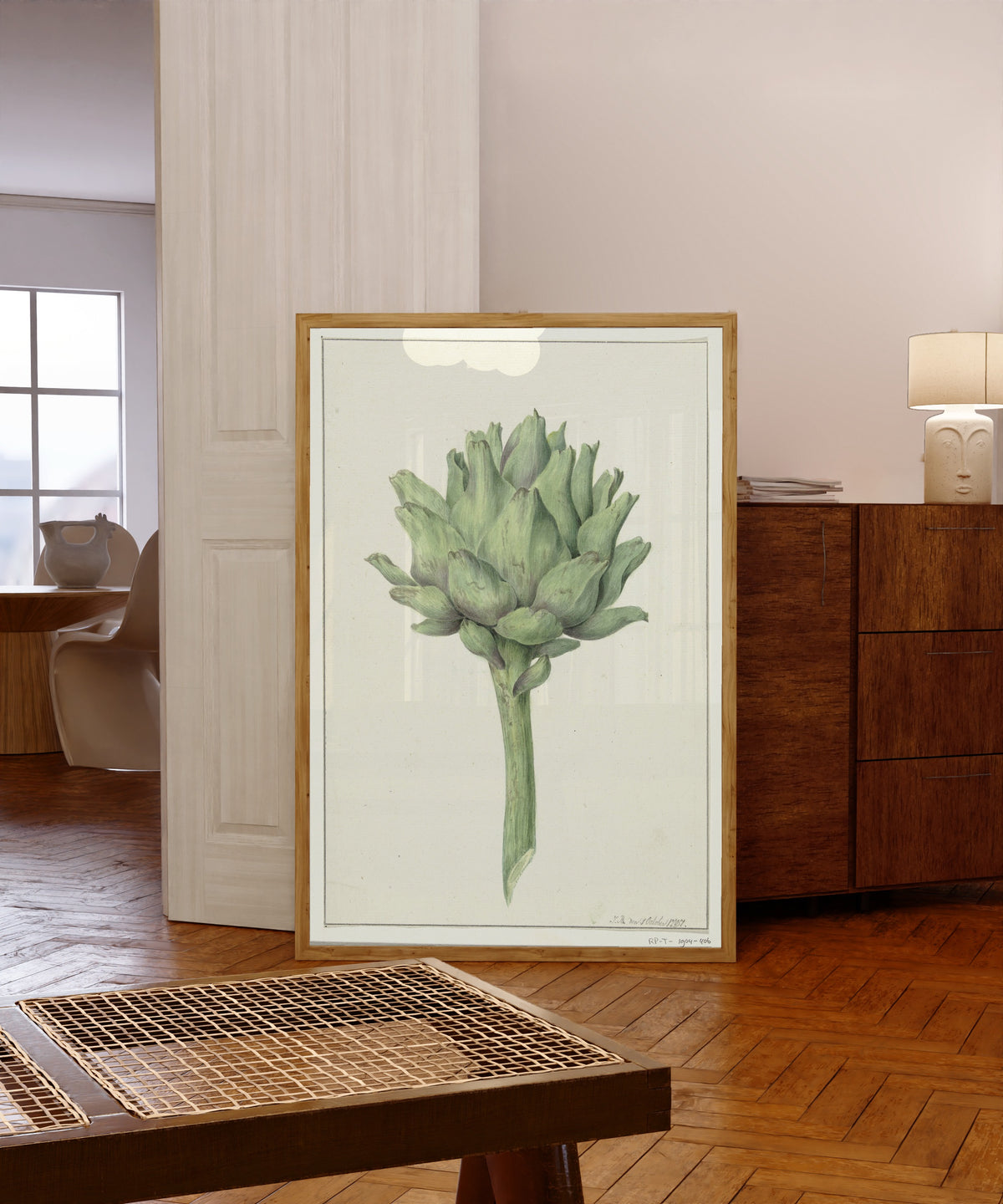 Framed art print of Artisjok (Artichoke) by Jean Bernard, in a light wood frame leaning in a warm room with a parquet floor