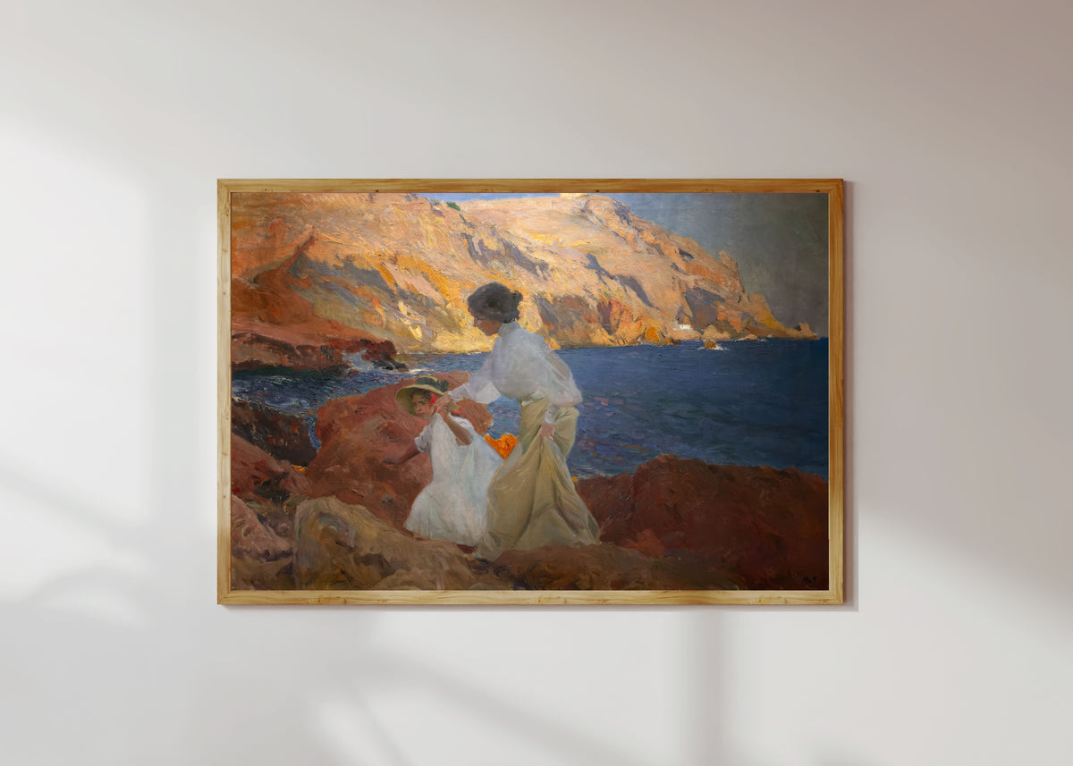 Framed art print of Clotilde and Elena on the Rocks, Jávea by Joaquín Sorolla, in a light wood frame on a sunlit white wall