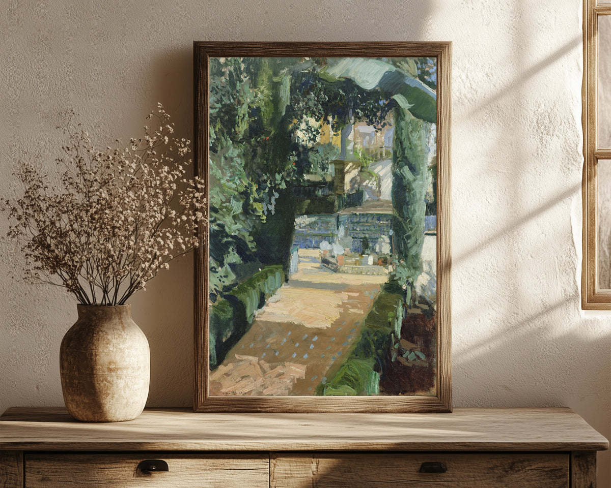 Framed art print of Court of the Dances, Alcázar of Seville by Joaquín Sorolla, in a dark wood frame leaning on a rustic console beside dried flowers