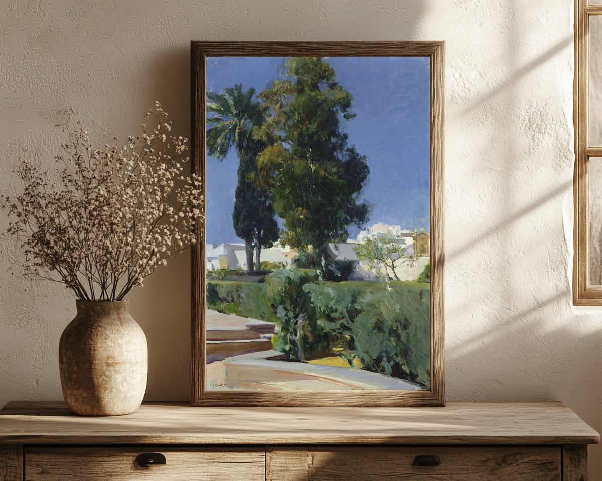 Framed art print of Gardens of the Alcázar, Seville by Joaquín Sorolla, in a dark wood frame leaning on a rustic console beside dried flowers