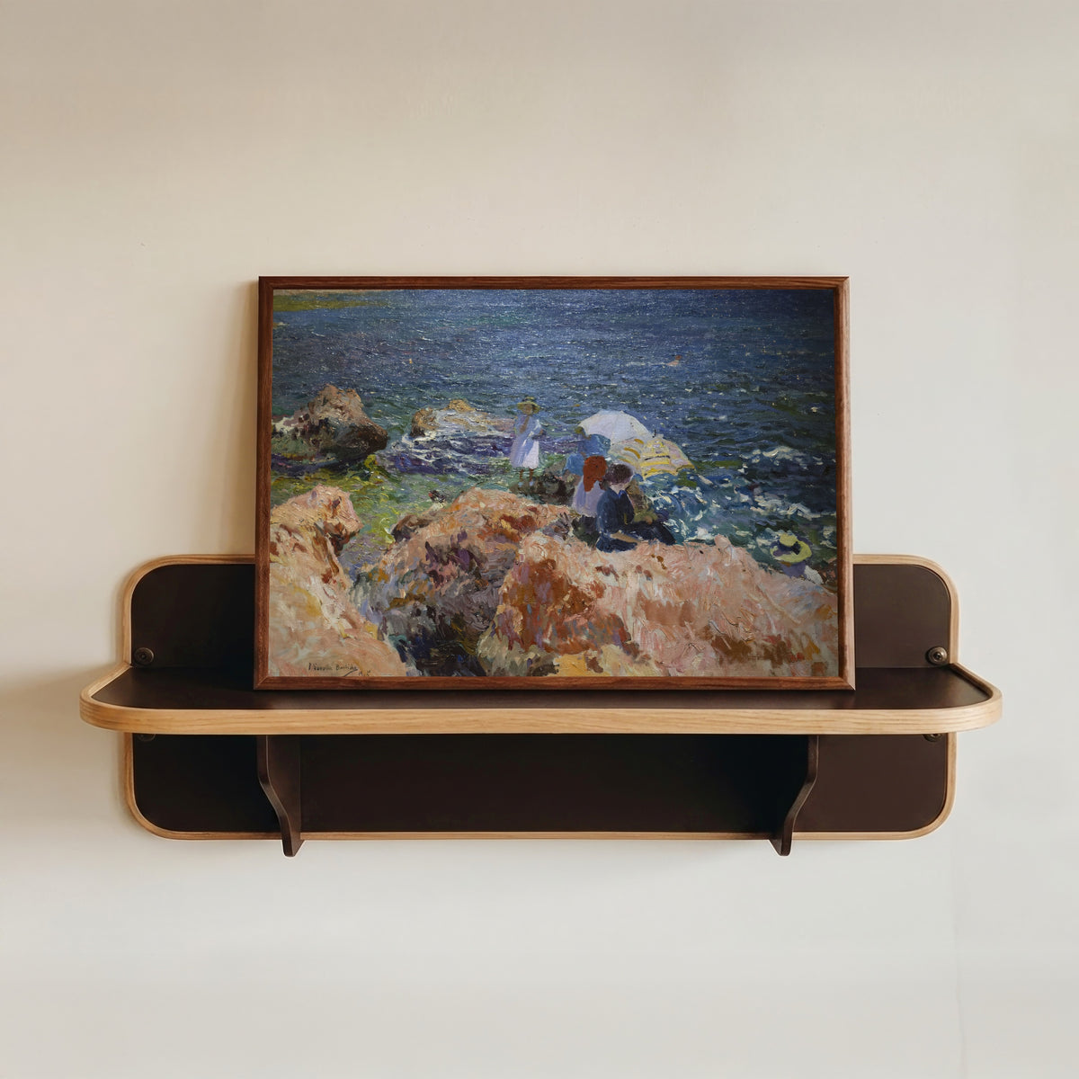 Framed art print of On the Rocks, Jávea by Joaquín Sorolla, in a dark wood frame resting on a wall shelf