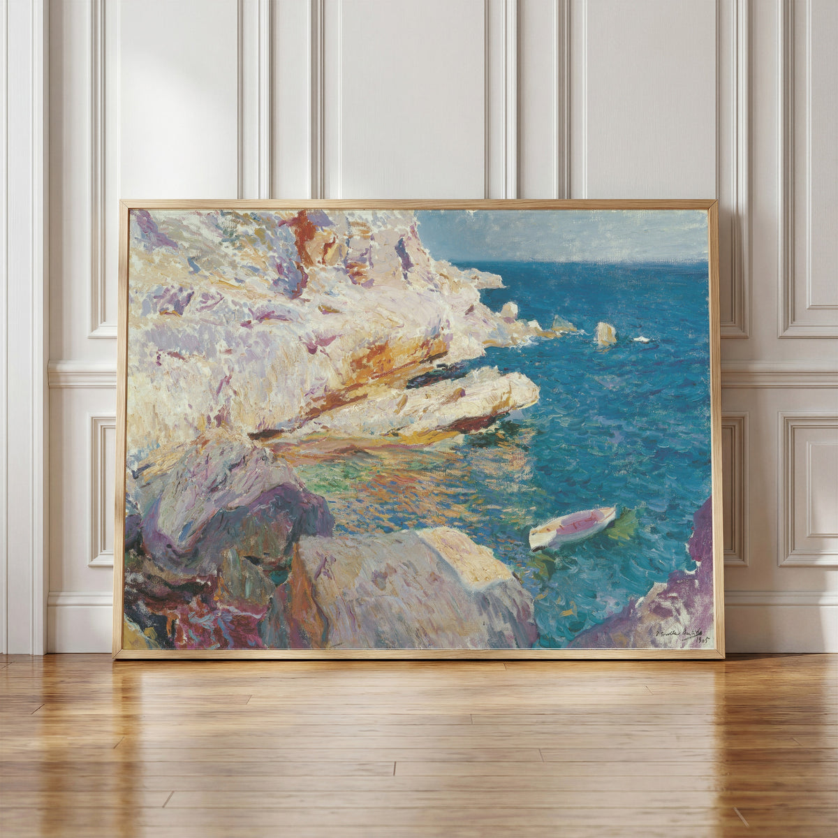 Framed art print of Rocks at Jávea and the White Boat by Joaquín Sorolla, in a light wood frame leaning against a panelled white wall
