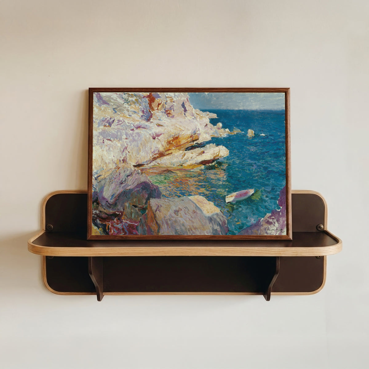 Framed art print of Rocks at Jávea and the White Boat by Joaquín Sorolla, in a dark wood frame resting on a wall shelf