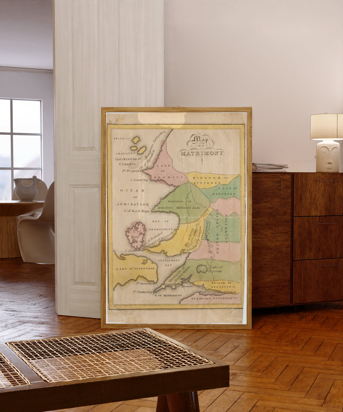 Framed art print of Map of Matrimony by John de Peyster Douw, in a light wood frame leaning in a warm room with a parquet floor