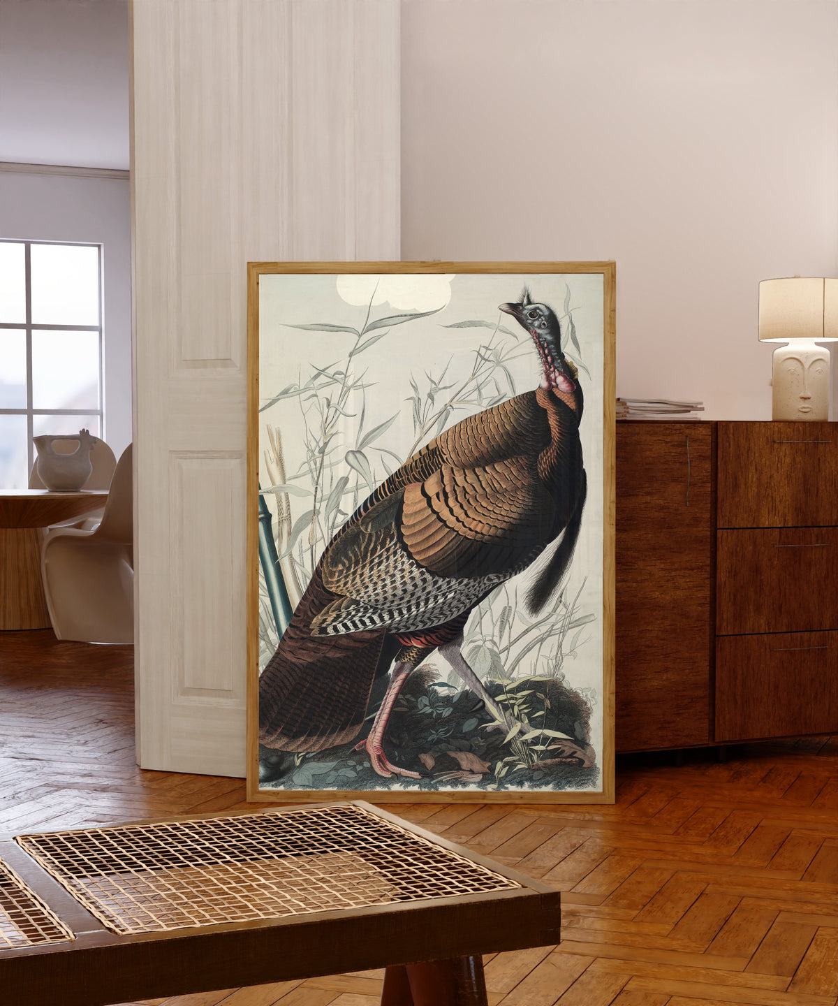 Framed art print of Wild Turkey by John James Audubon, in a light wood frame leaning in a warm room with a parquet floor