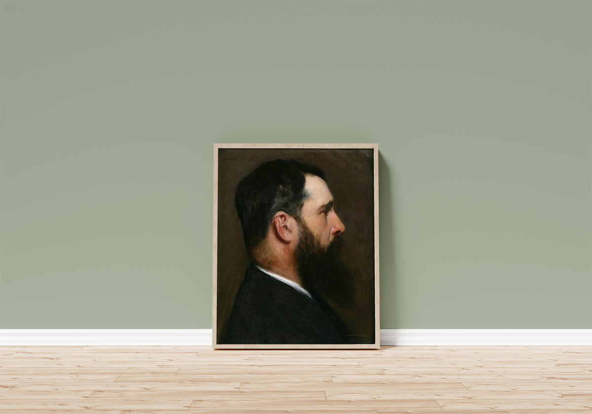 Framed art print of Claude Monet by John Singer Sargent, in a light wood frame leaning on a sage green wall above a wooden floor