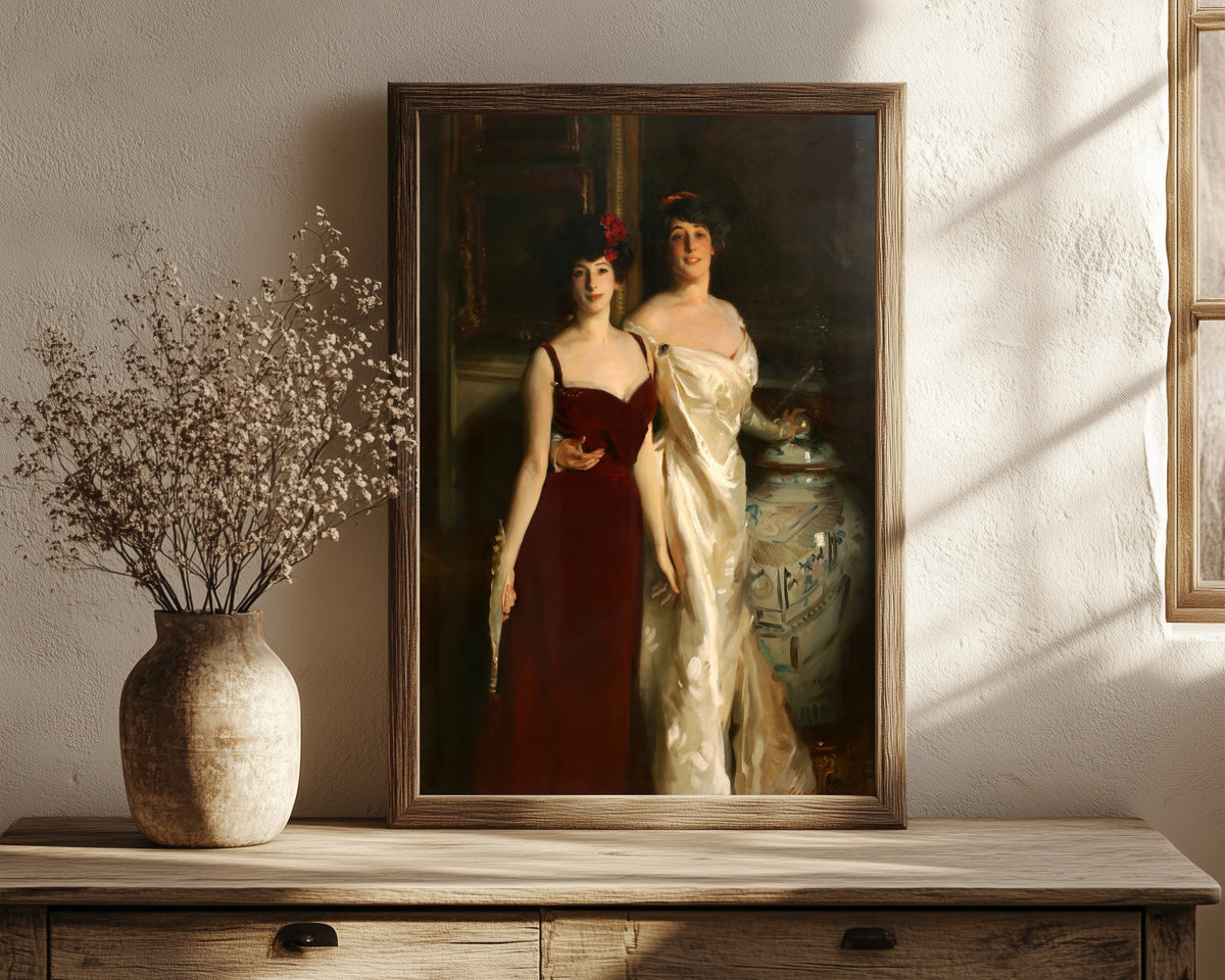 Framed art print of Ena and Betty, Daughters of Asher and Mrs.… by John Singer Sargent, in a dark wood frame leaning on a rustic console beside dried flowers
