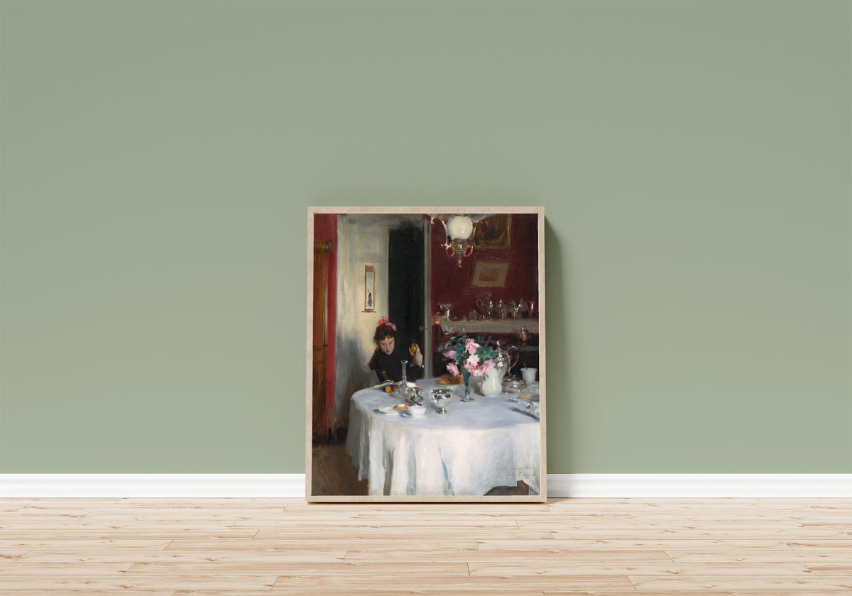 Framed art print of The Breakfast Table by John Singer Sargent, in a light wood frame leaning on a sage green wall above a wooden floor