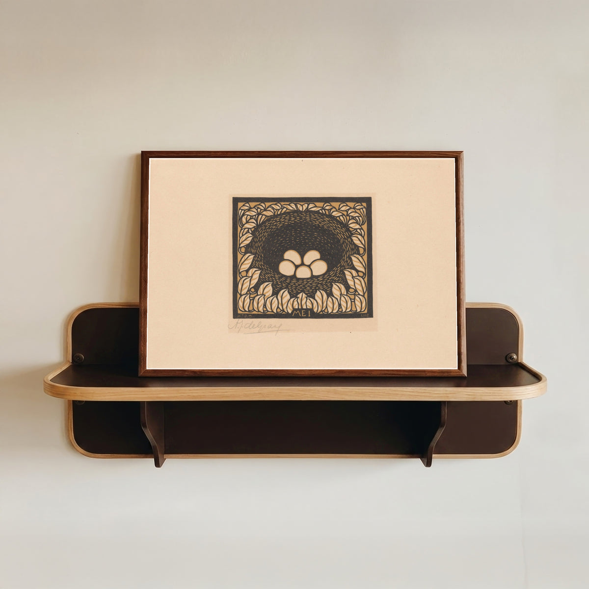 Framed art print of Bird's nest with eggs by Julie de Graag, in a dark wood frame resting on a wall shelf