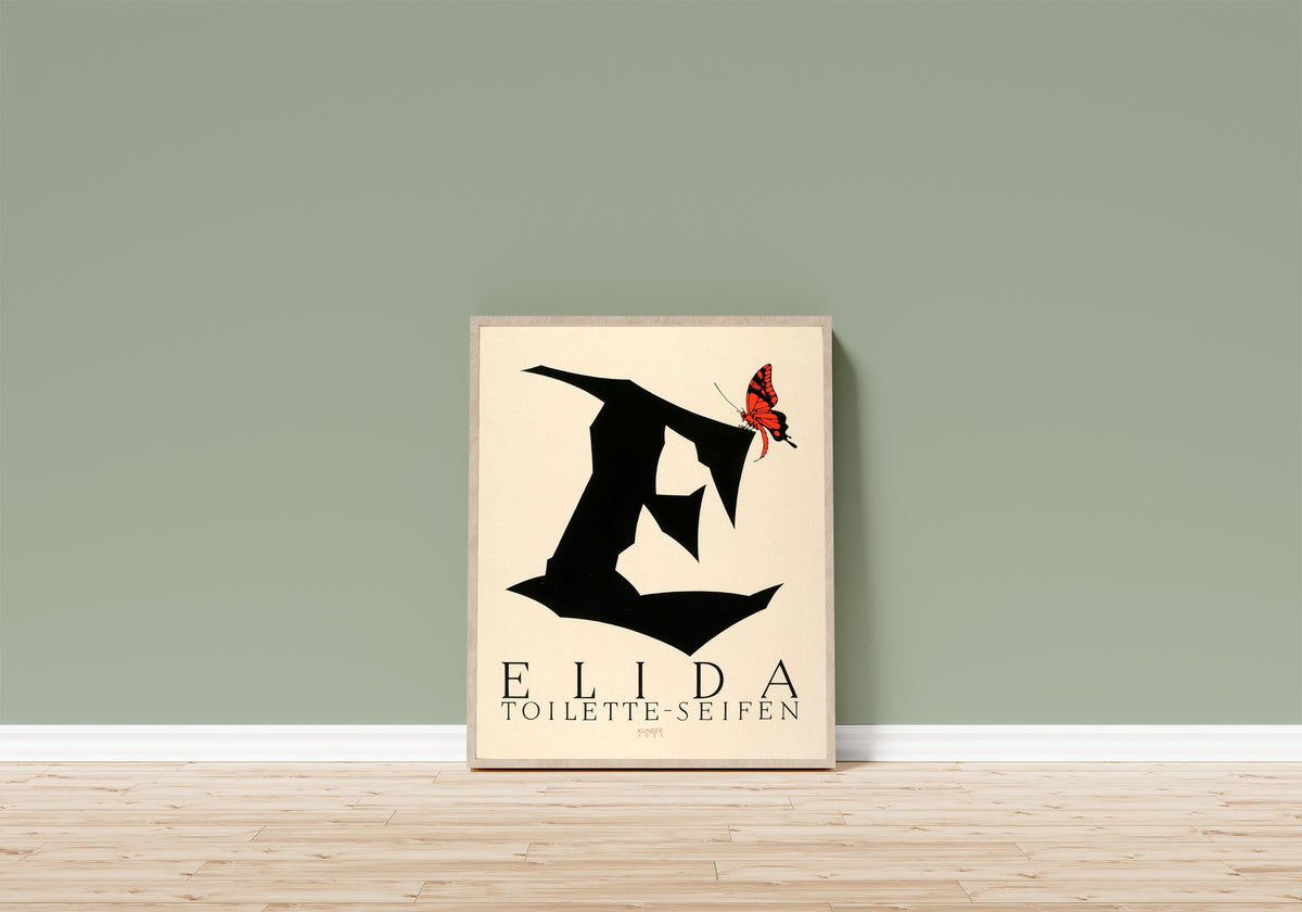 Framed art print of Elida Toilette-Seifen by Julius Klinger, in a light wood frame leaning on a sage green wall above a wooden floor