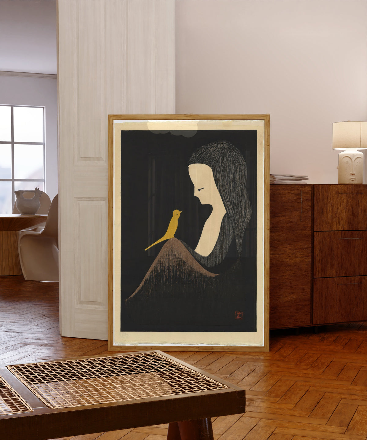 Framed art print of Girl with Yellow Bird by Kaoru Kawano, in a light wood frame leaning in a warm room with a parquet floor
