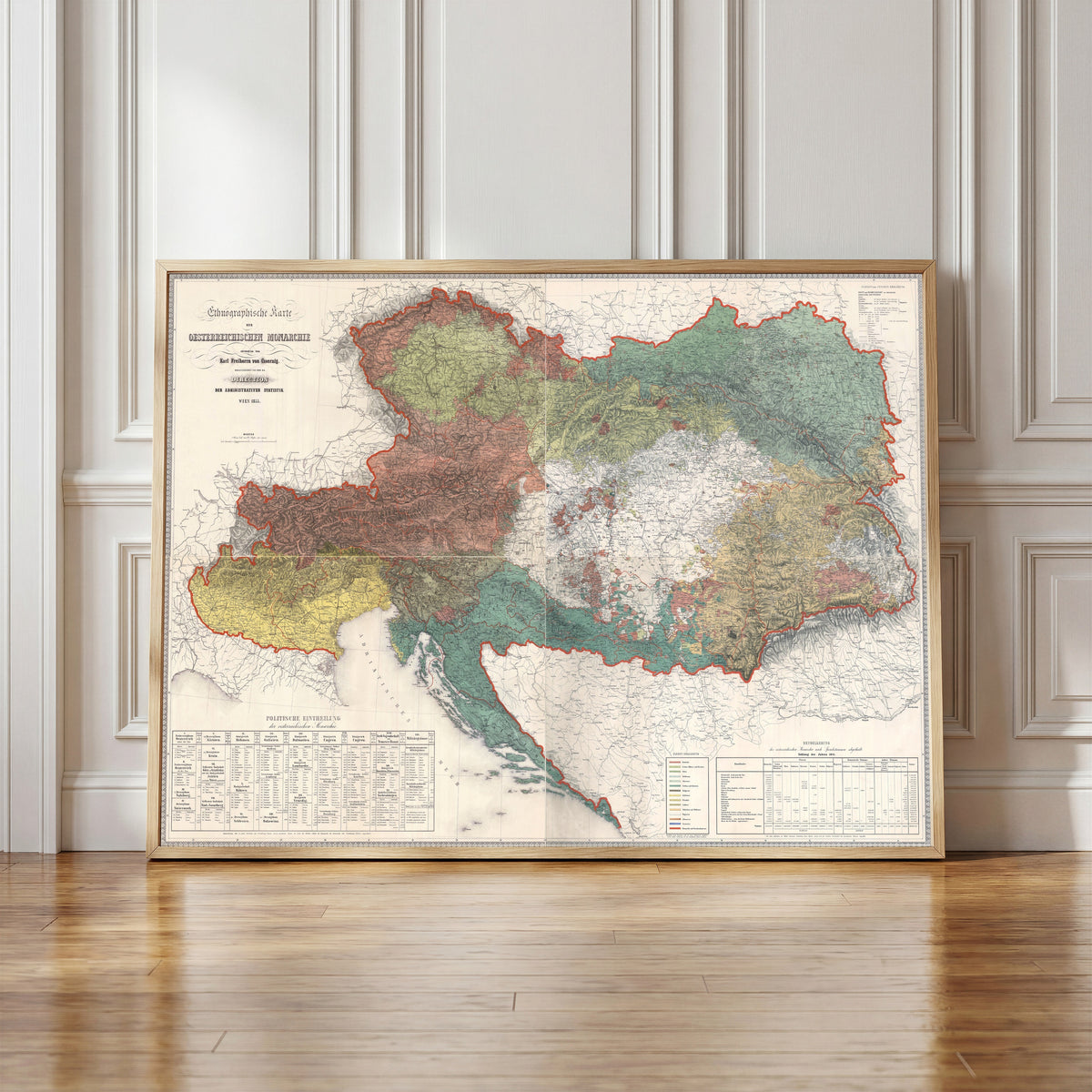 Framed art print of Ethnographic Map of the Austrian Monarchy by Karl von Czoernig, in a light wood frame leaning against a panelled white wall