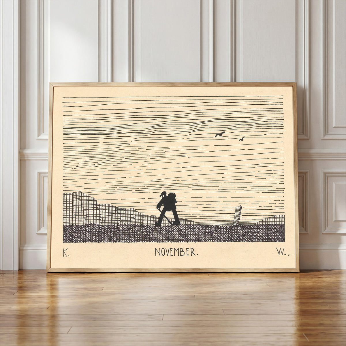 Framed art print of November by Karl Wiener, in a light wood frame leaning against a panelled white wall