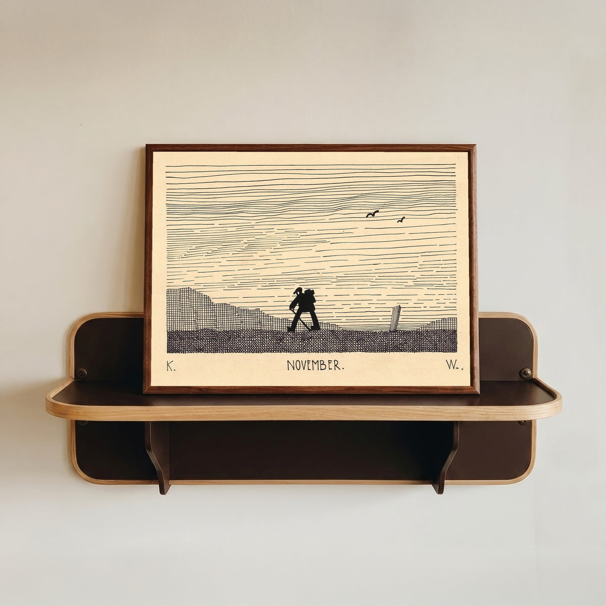 Framed art print of November by Karl Wiener, in a dark wood frame resting on a wall shelf
