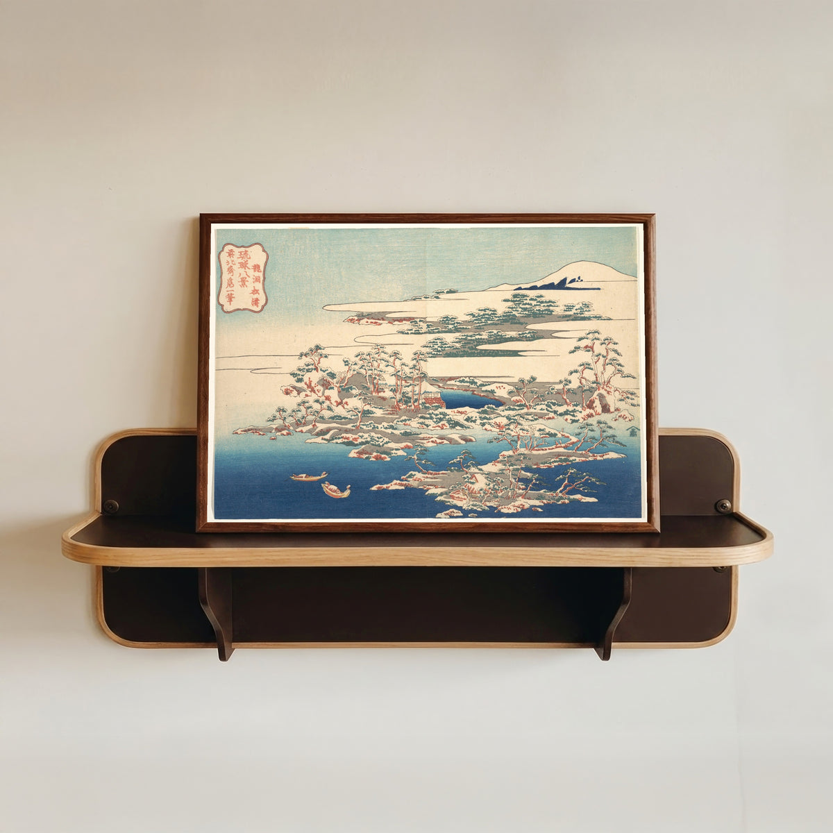 Framed art print of Eight Views of the Ryūkyū Islands: Pines and Waves at Ryūtō by Katsushika Hokusai, in a dark wood frame resting on a wall shelf