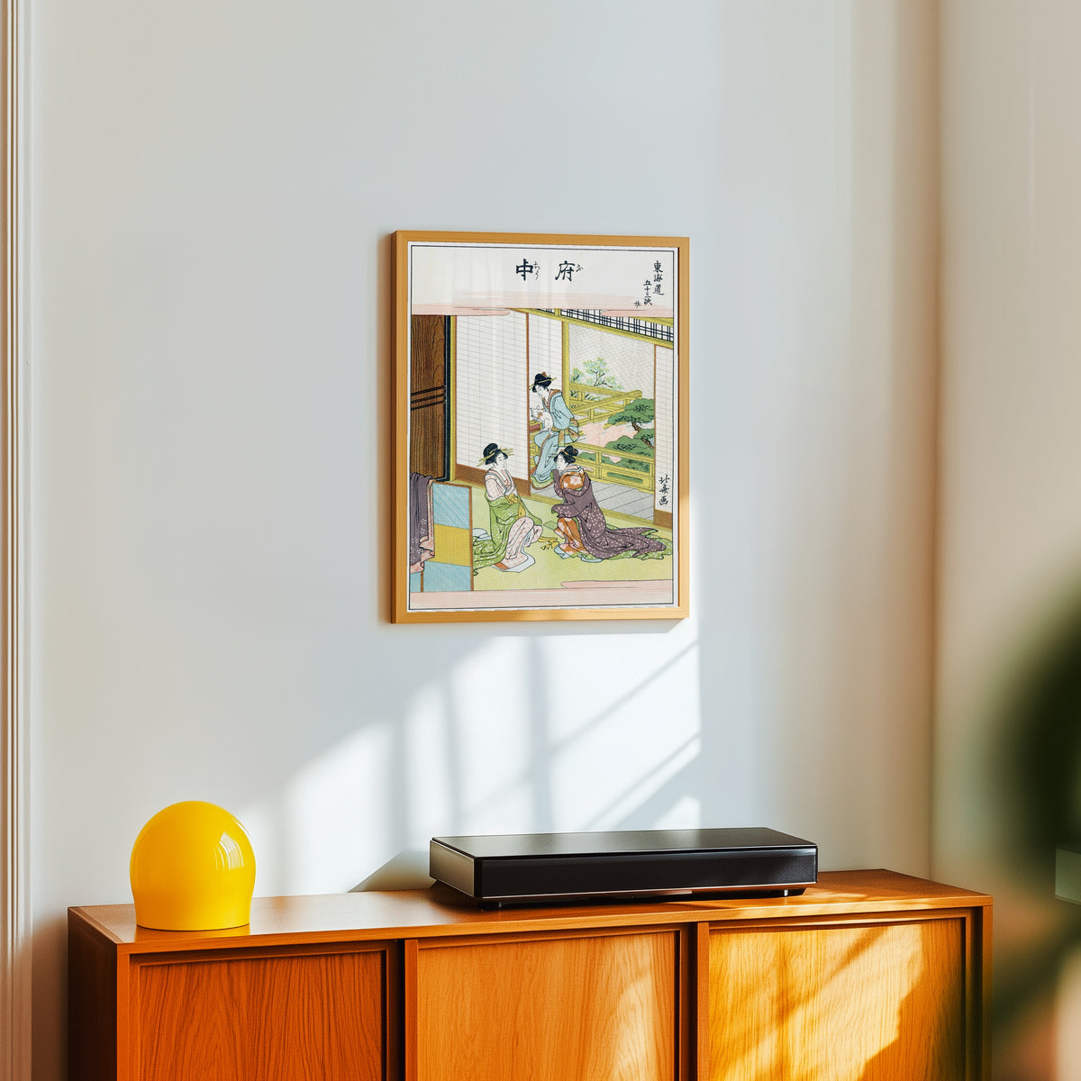 Framed art print of Fifty-three Stations of the Tokaido: Fuchu by Katsushika Hokusai, in a light wood frame on a white wall above an orange sideboard