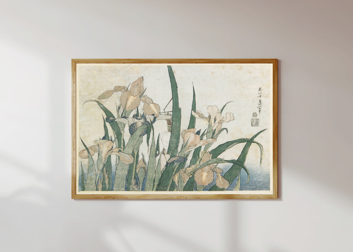 Framed art print of Large Flowers: Irises and Grasshopper by Katsushika Hokusai, in a light wood frame on a sunlit white wall