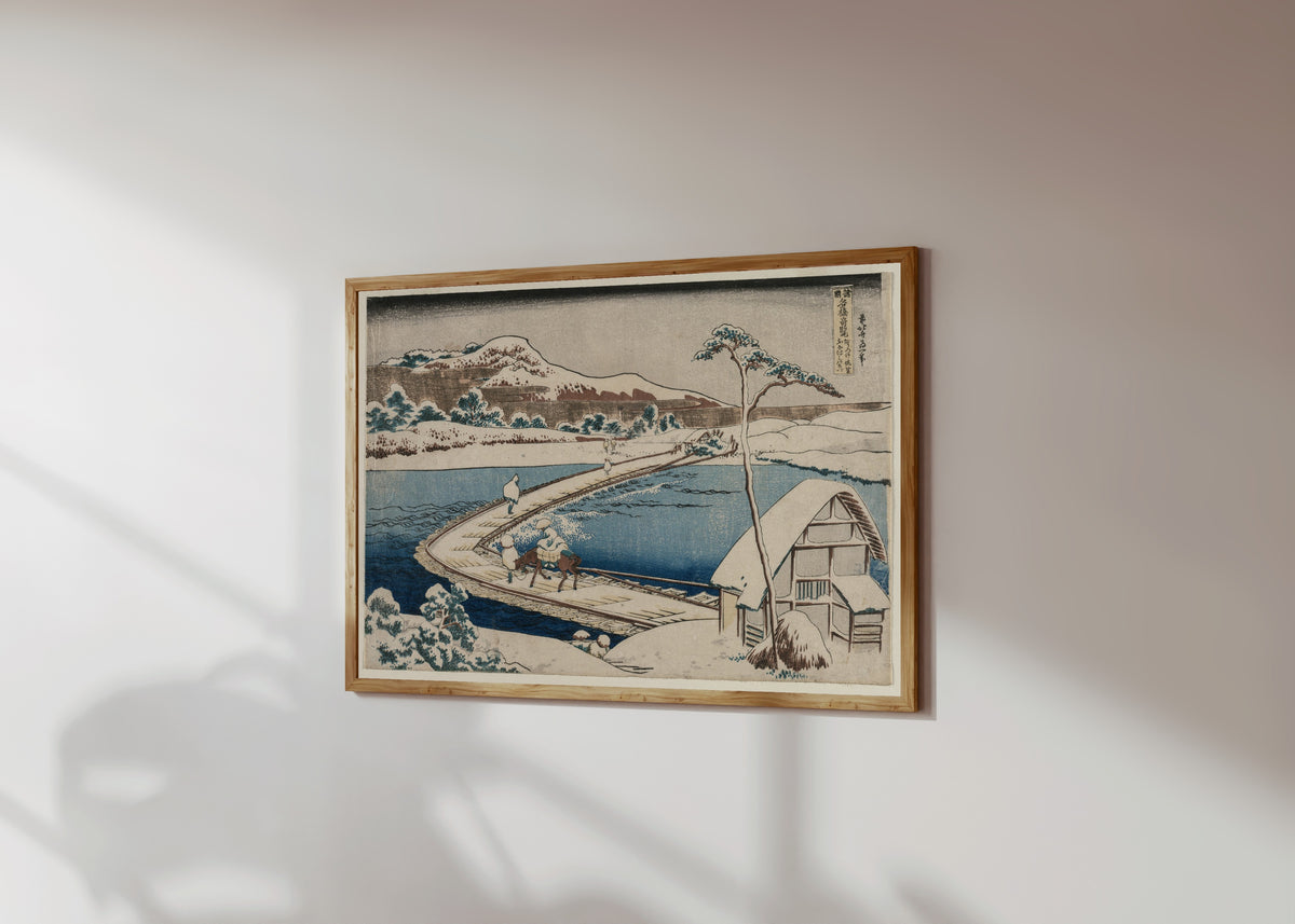 Framed art print of Remarkable Views of Bridges in Various… by Katsushika Hokusai, in a light wood frame on a sunlit white wall, seen at a slight angle