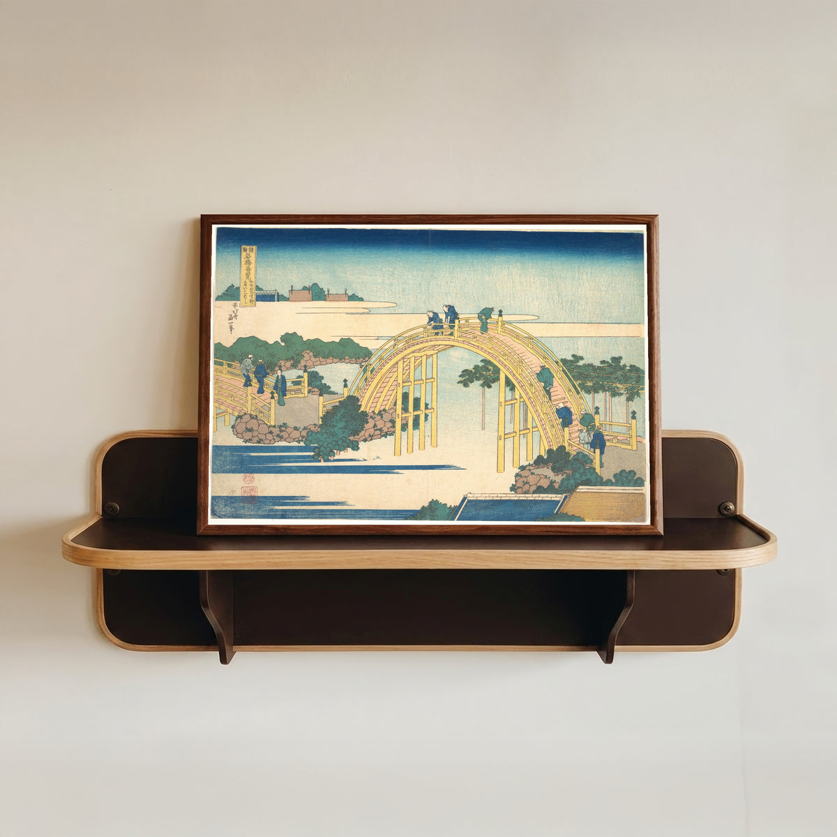Framed art print of Remarkable Views of Bridges in Various Provinces: The Arched Bridge at… by Katsushika Hokusai, in a dark wood frame resting on a wall shelf
