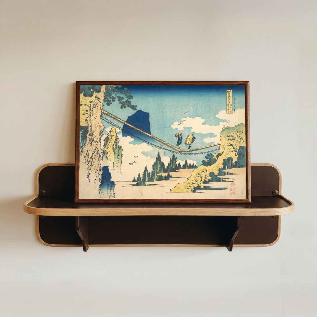Framed art print of Remarkable Views of Bridges in Various Provinces: The Suspension… by Katsushika Hokusai, in a dark wood frame resting on a wall shelf
