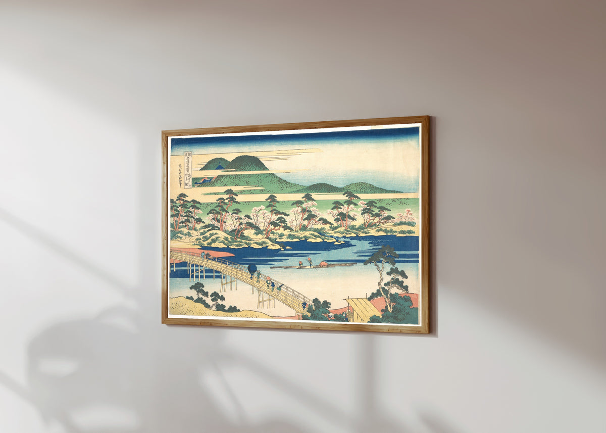 Framed art print of Remarkable Views of Bridges in Various… by Katsushika Hokusai, in a light wood frame on a sunlit white wall, seen at a slight angle