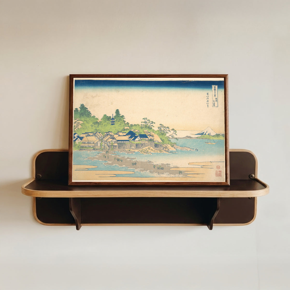Framed art print of Thirty-six Views of Mount Fuji: Enoshima Island in Sagami Province by Katsushika Hokusai, in a dark wood frame resting on a wall shelf
