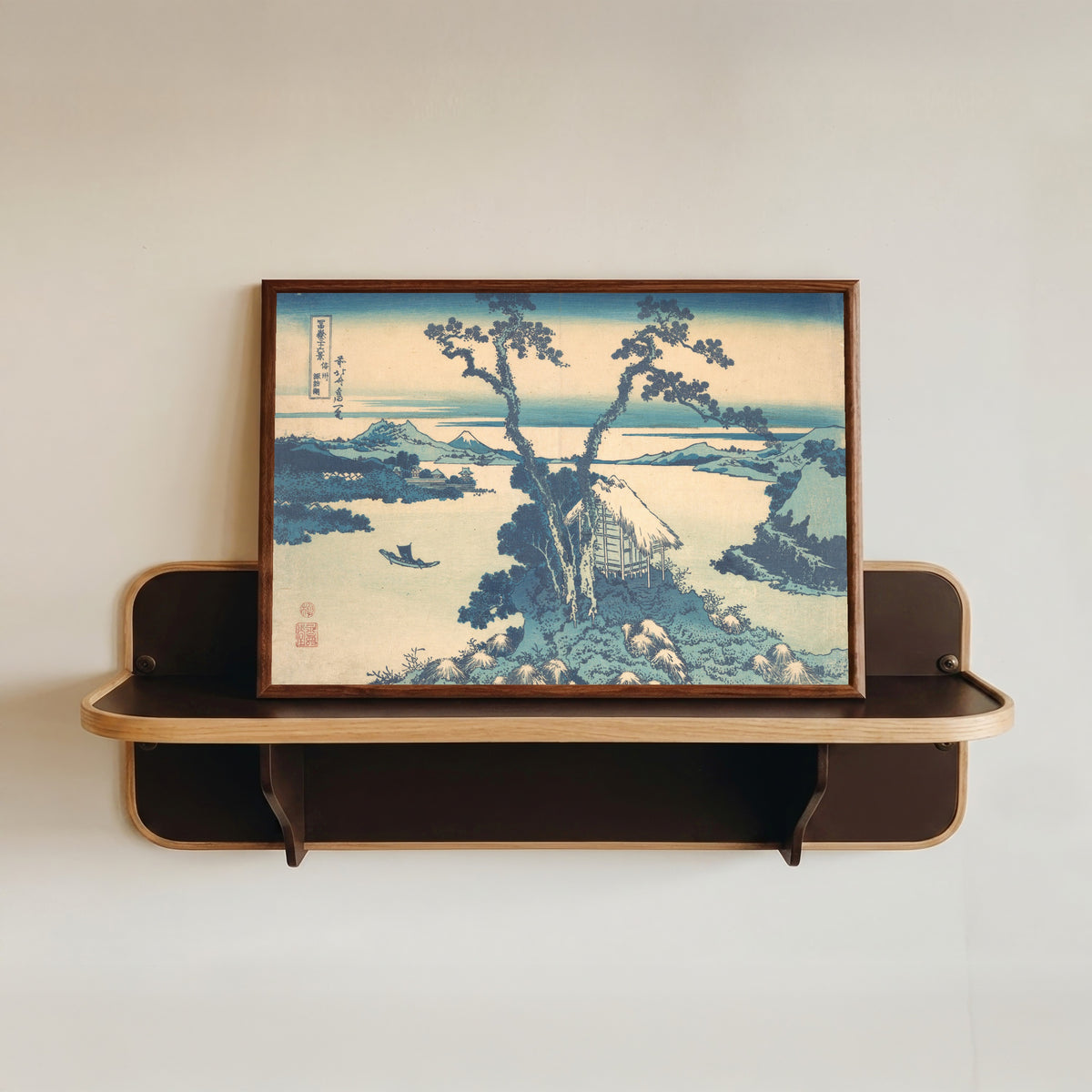 Framed art print of Thirty-six Views of Mount Fuji: Lake Suwa in Shinano Province by Katsushika Hokusai, in a dark wood frame resting on a wall shelf
