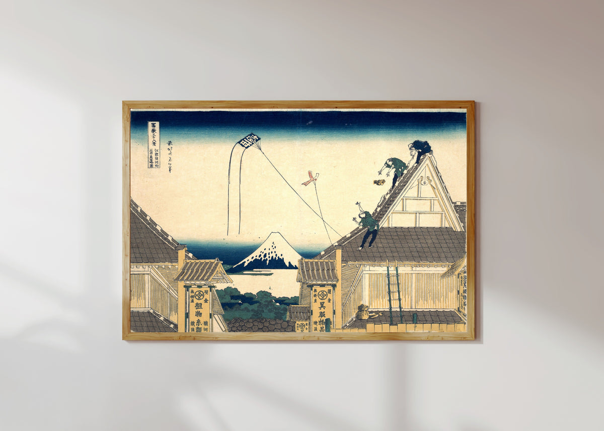 Framed art print of Thirty-six Views of Mount Fuji: Mitsui Shop at Surugachō in Edo by Katsushika Hokusai, in a light wood frame on a sunlit white wall