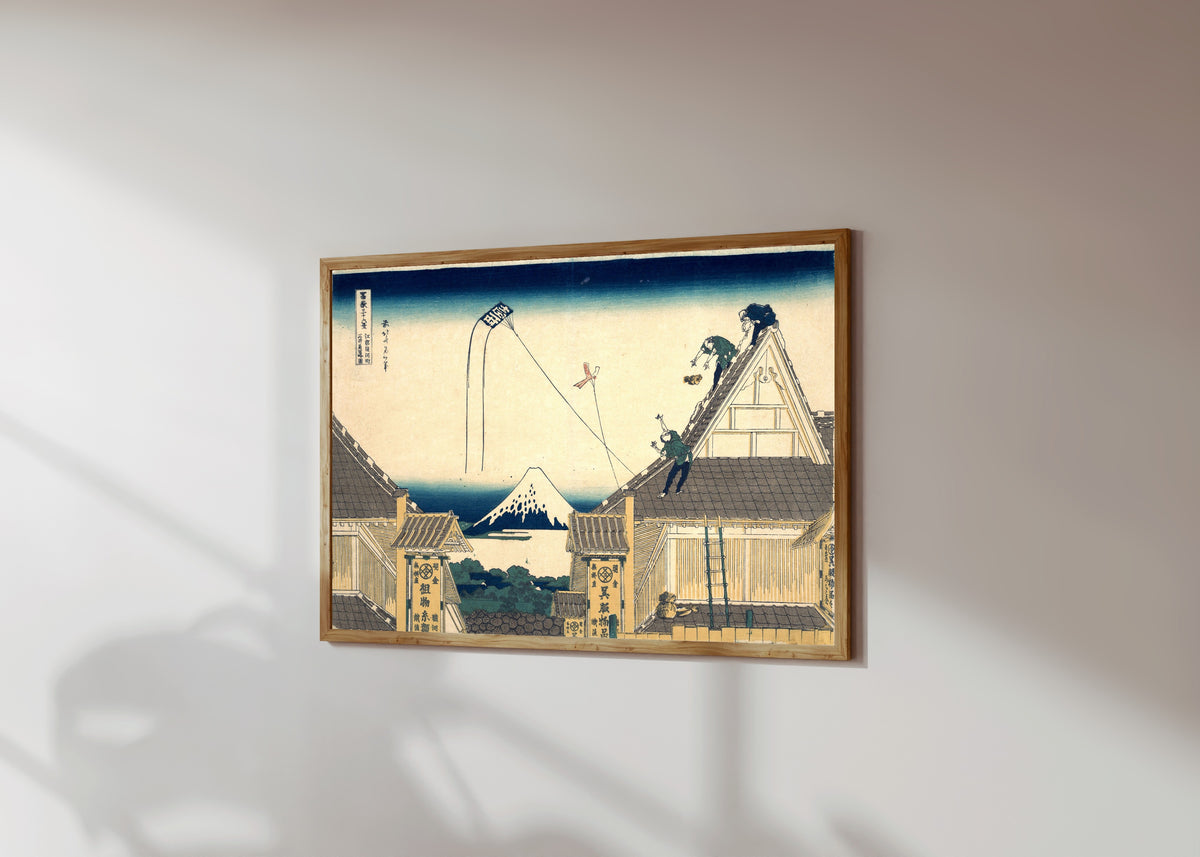 Framed art print of Thirty-six Views of Mount Fuji: Mitsui Shop at… by Katsushika Hokusai, in a light wood frame on a sunlit white wall, seen at a slight angle
