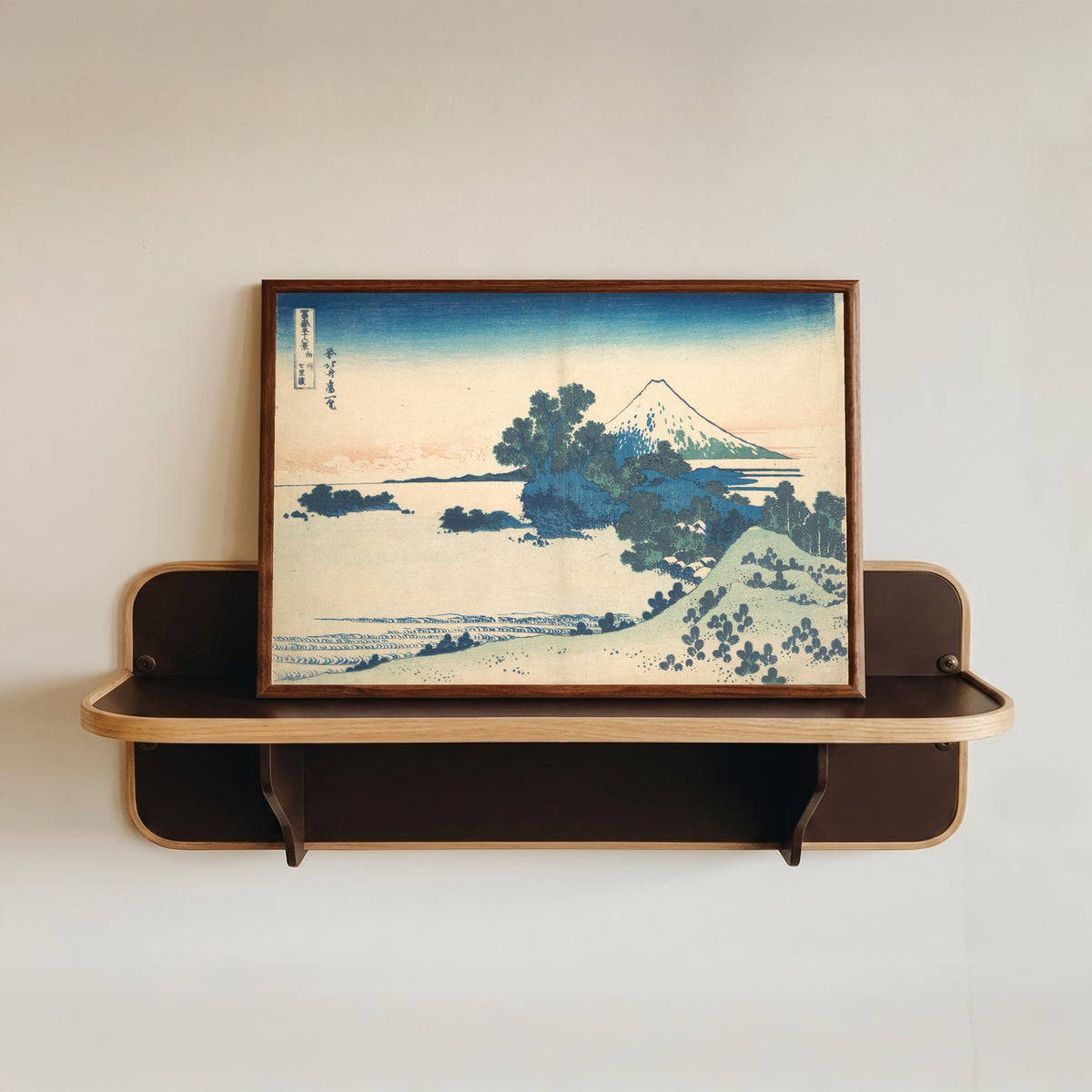 Framed art print of Thirty-six Views of Mount Fuji: Shichirigahama in Sagami Province by Katsushika Hokusai, in a dark wood frame resting on a wall shelf