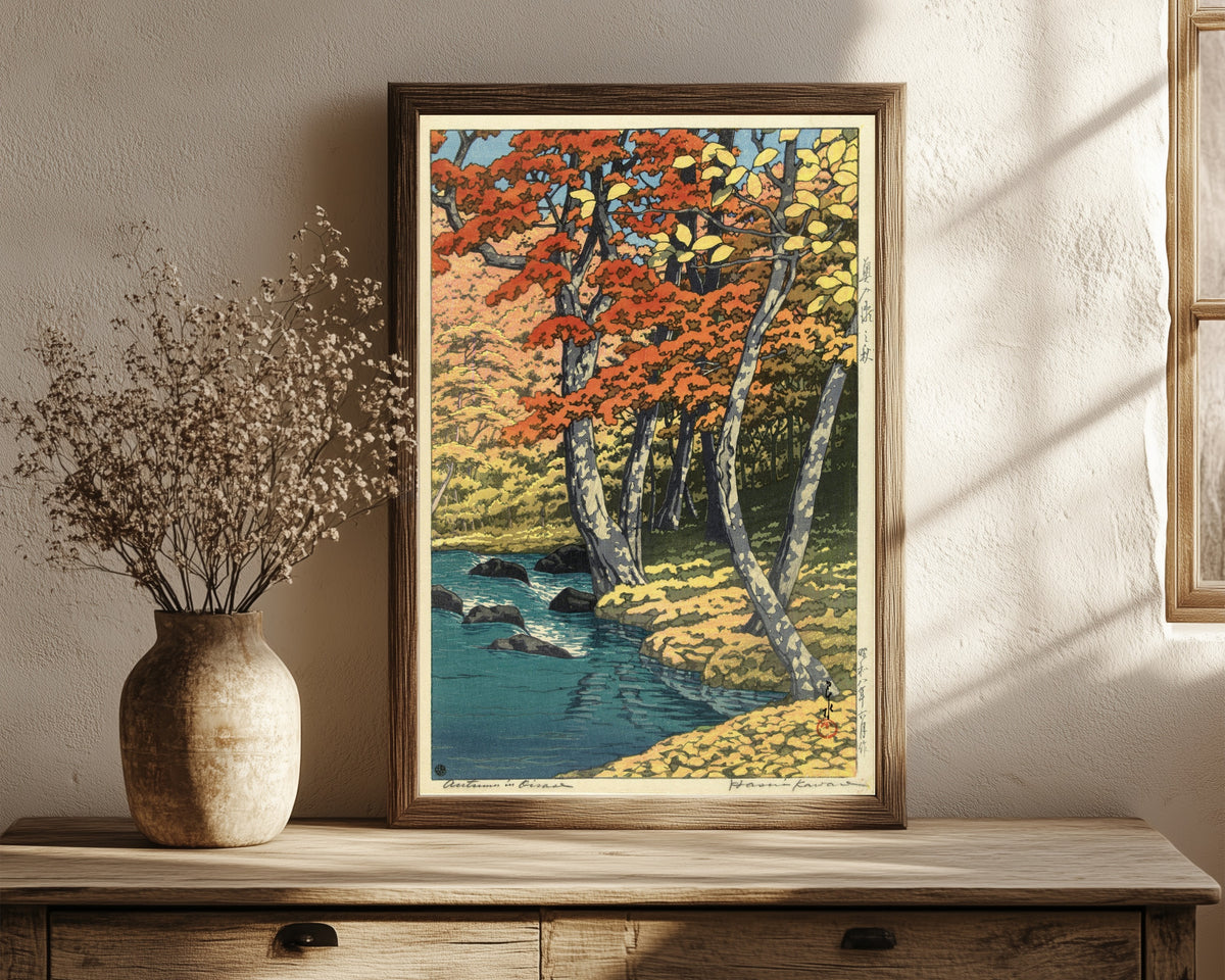 Framed art print of Autumn in the Forest by Kawase Hasui, in a dark wood frame leaning on a rustic console beside dried flowers