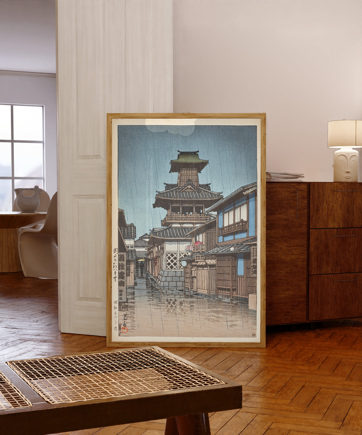 Framed art print of Bell Tower at Okayama by Kawase Hasui, in a light wood frame leaning in a warm room with a parquet floor