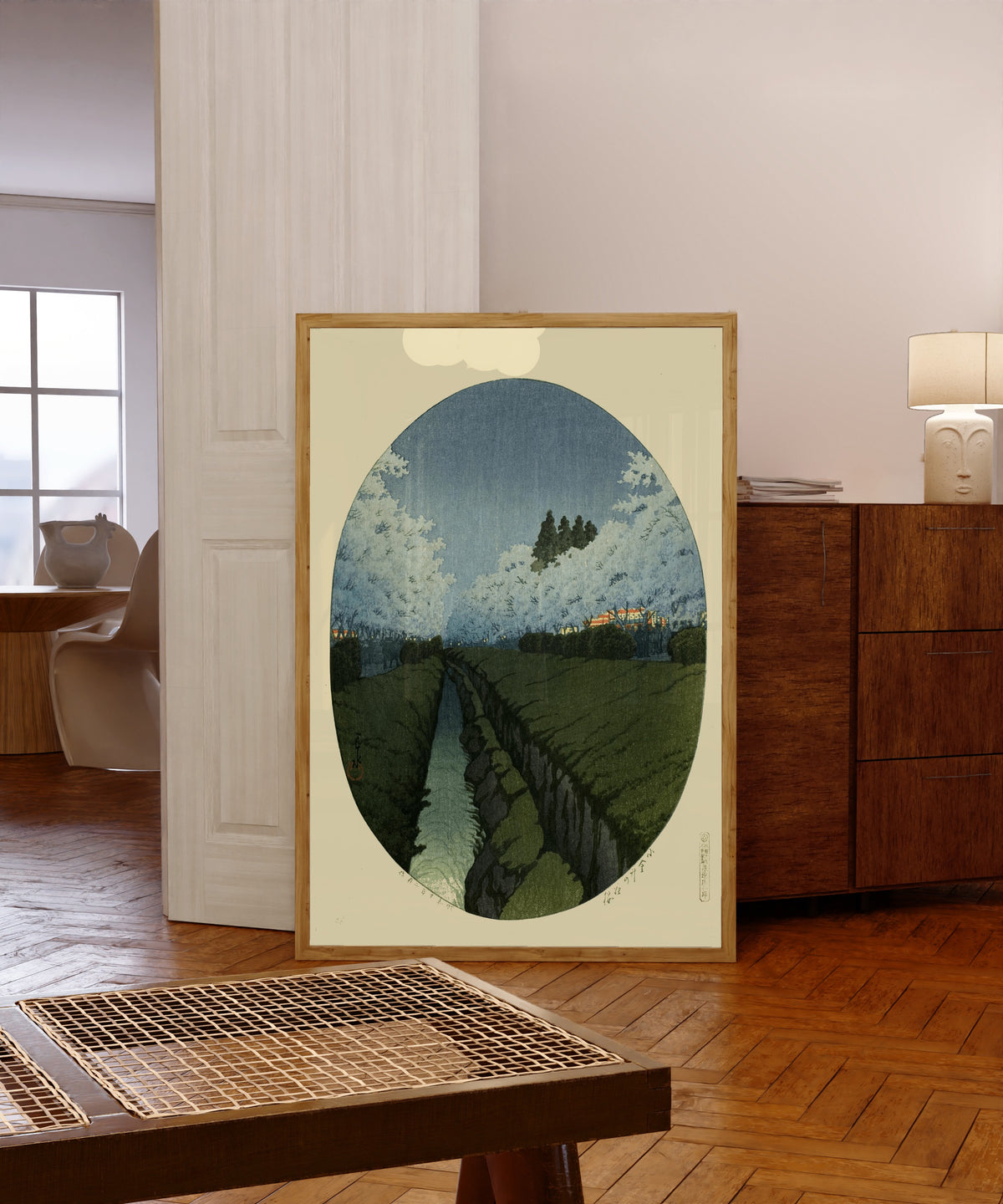 Framed art print of Cherry Blossoms at Koganei, Night by Kawase Hasui, in a light wood frame leaning in a warm room with a parquet floor