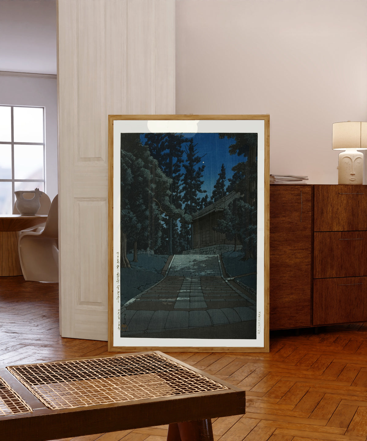 Framed art print of Konjikido at Chusonji, Hiraizumi, at Night by Kawase Hasui, in a light wood frame leaning in a warm room with a parquet floor