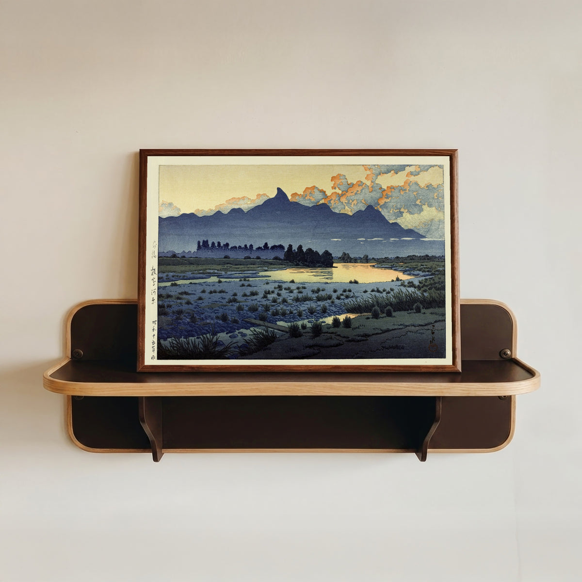 Framed art print of Maebashi Marshes by Kawase Hasui, in a dark wood frame resting on a wall shelf